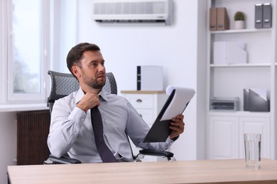 Image of Worker feeling hot at table in office. Broken or incorrectly adjusted air conditioner