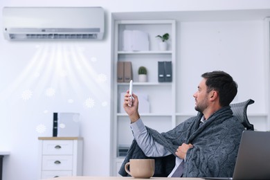 Image of Worker wrapped in blanket using remote control at table in office. Broken or incorrectly adjusted air conditioner