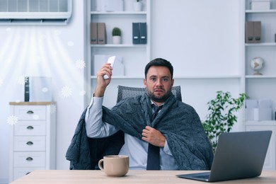 Image of Worker wrapped in blanket using remote control at table in office. Broken or incorrectly adjusted air conditioner