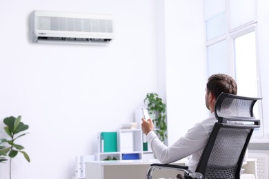 Image of Man using remote control to turn on air conditioner in office