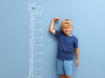 Image of Cute little boy measuring his height near blue wall with scale and drawing of giraffe