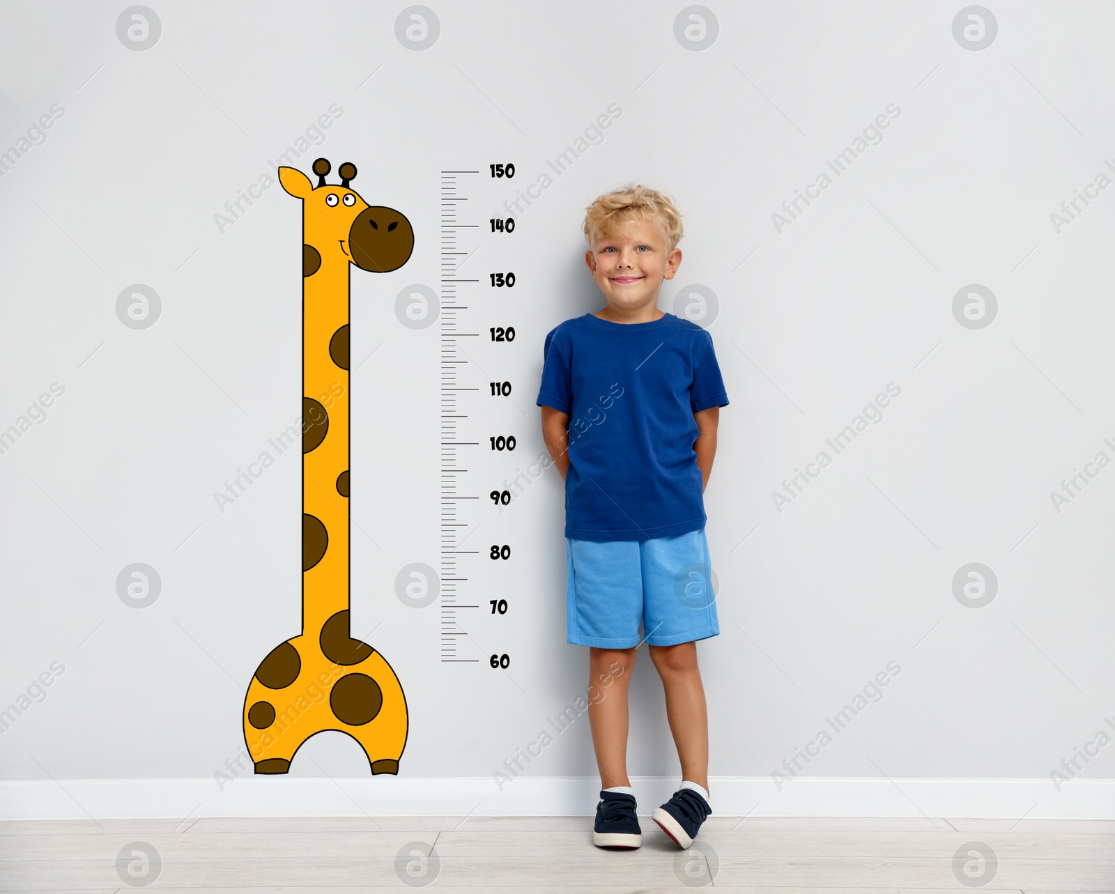 Image of Cute little boy measuring his height near white wall with scale and drawing of giraffe