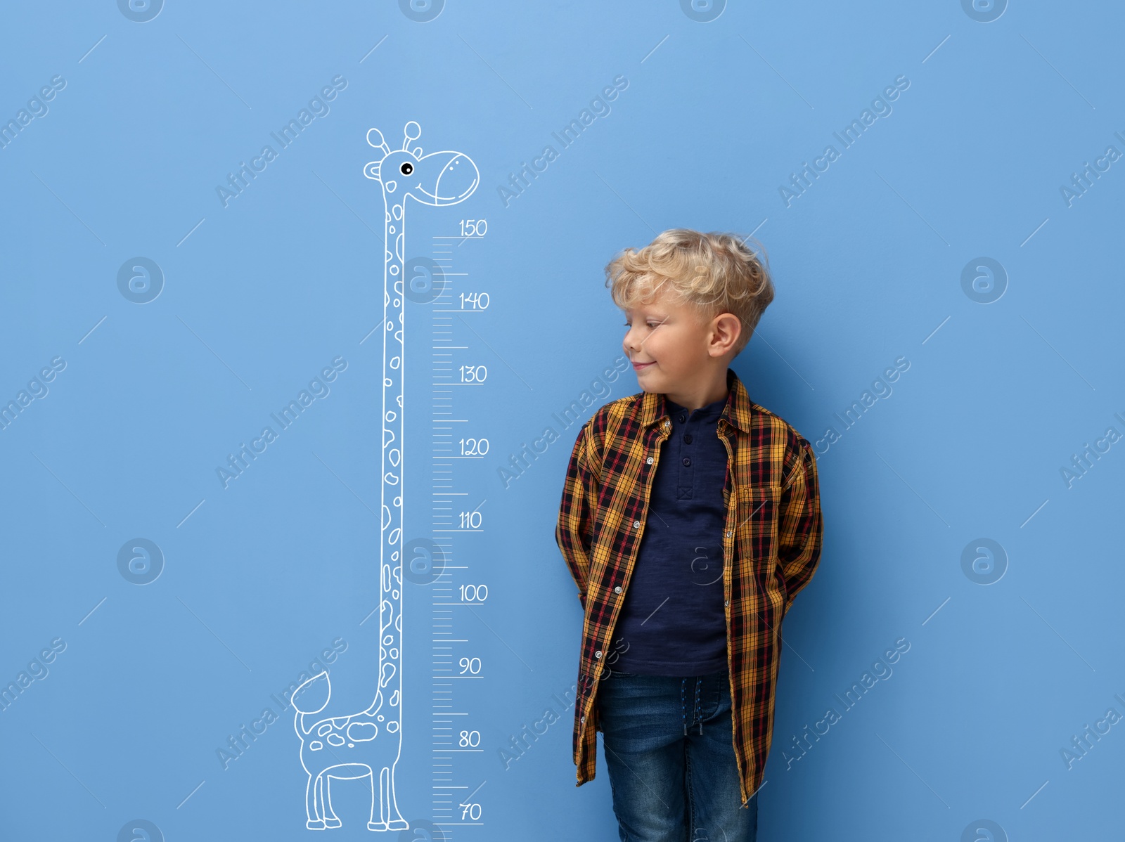 Image of Cute little boy measuring his height near blue wall with scale and drawing of giraffe
