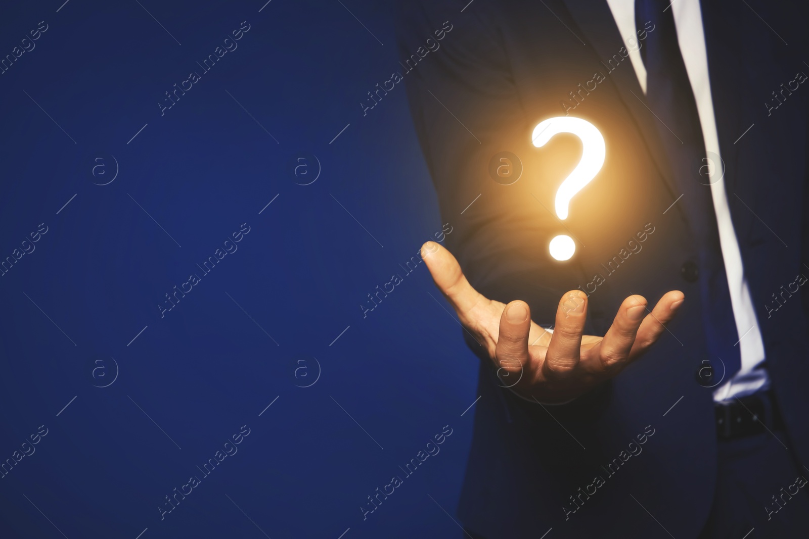 Image of Businessman holding question mark against dark blue background, closeup