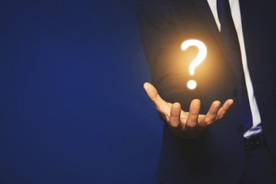 Image of Businessman holding question mark against dark blue background, closeup