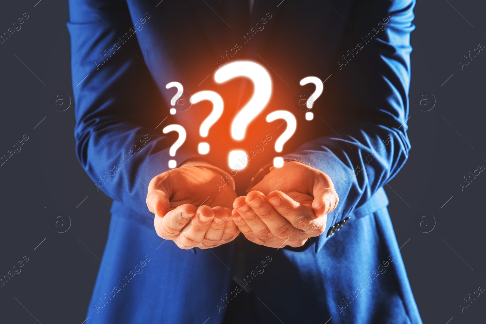 Image of Businessman holding question marks against dark grey background, closeup