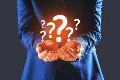Image of Businessman holding question marks against dark grey background, closeup
