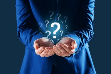 Image of Businessman holding question mark against dark blue background, closeup