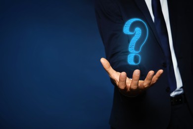 Image of Businessman holding question mark against dark blue background, closeup