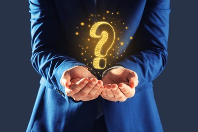 Image of Businessman holding question mark against dark grey background, closeup