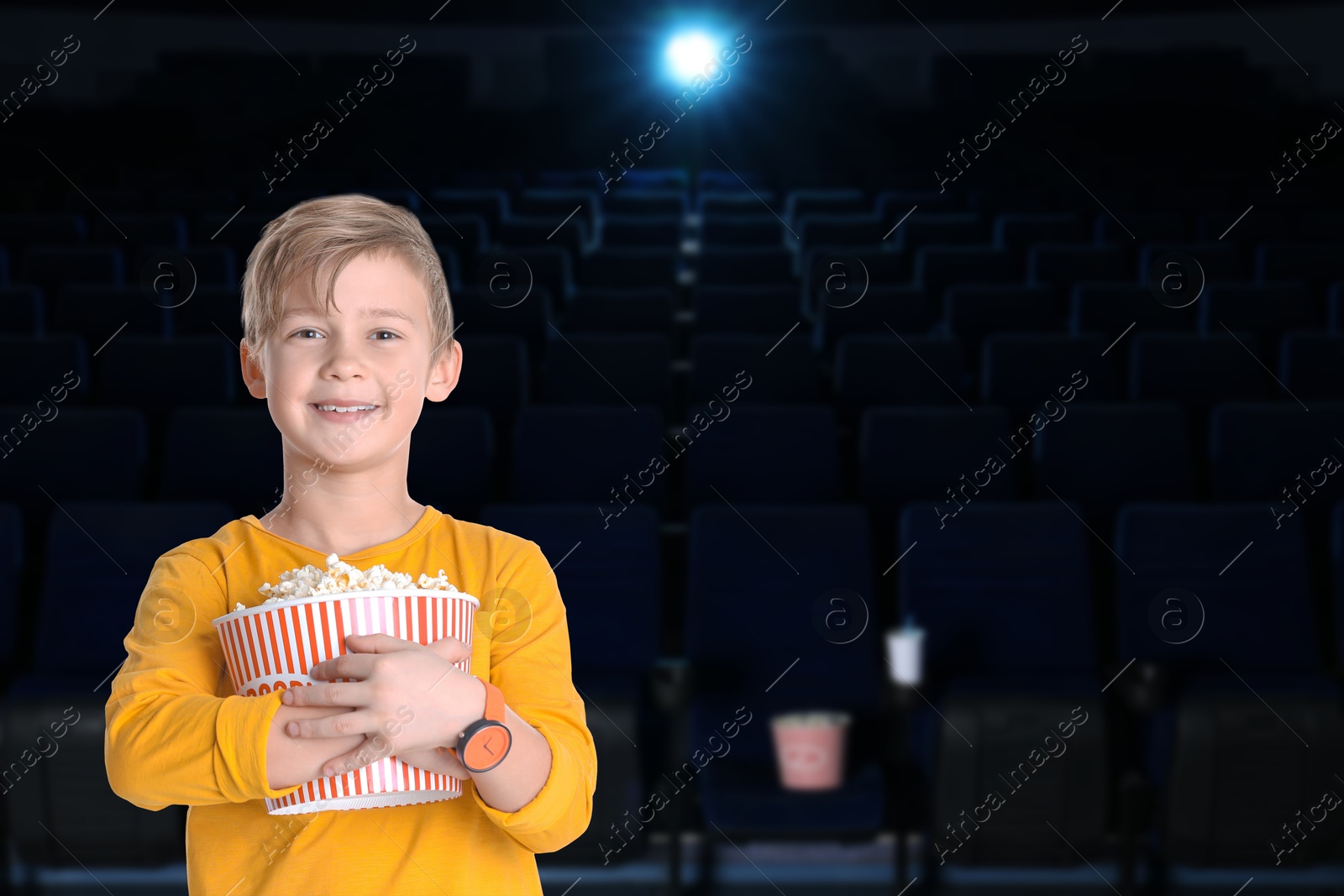 Image of Happy little boy with big bucket of popcorn in dark cinema