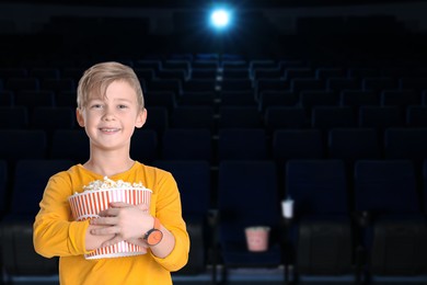 Image of Happy little boy with big bucket of popcorn in dark cinema