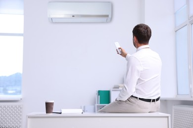 Image of Man switching on air conditioner with remote control in office