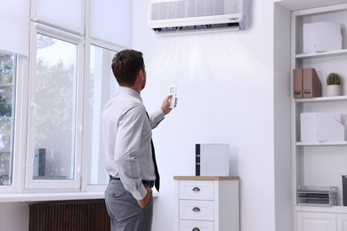 Image of Man switching on air conditioner with remote control in office