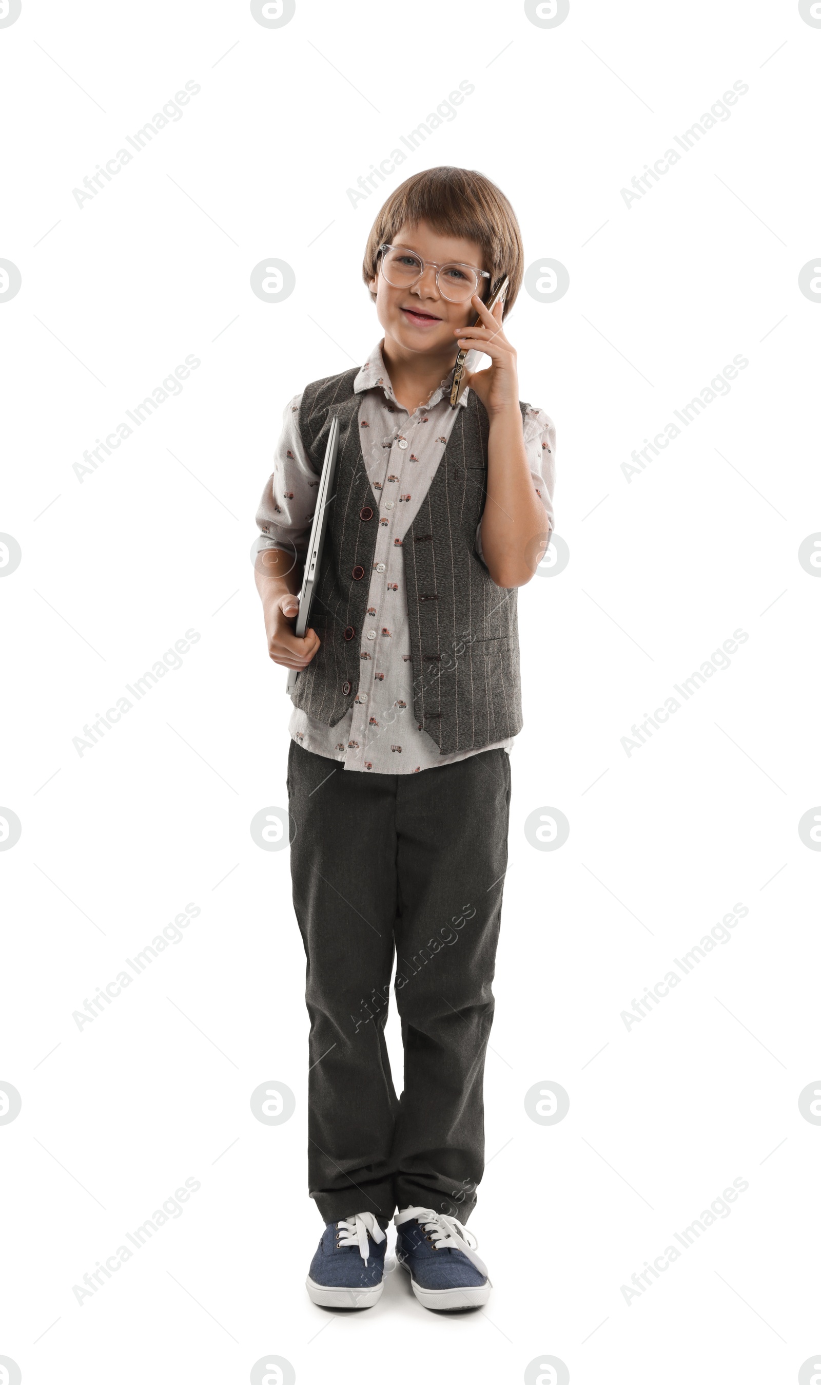 Photo of Choice of profession. Happy little boy in glasses talking by smartphone pretending to work with laptop on white background