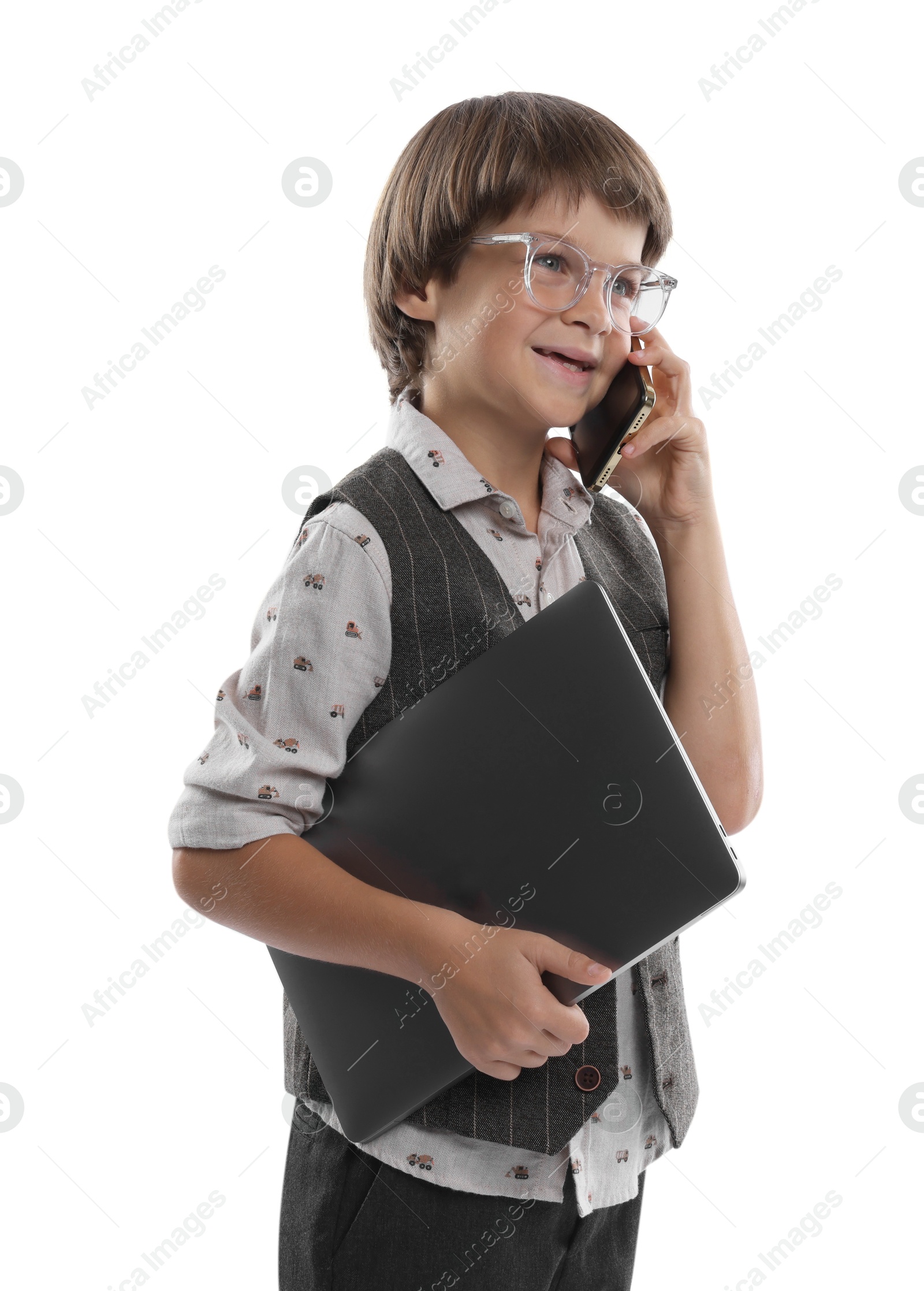 Photo of Choice of profession. Happy little boy in glasses talking by smartphone pretending to work with laptop on white background