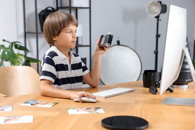 Photo of Choice of profession. Little boy with camera pretending to be photographer at wooden table in studio