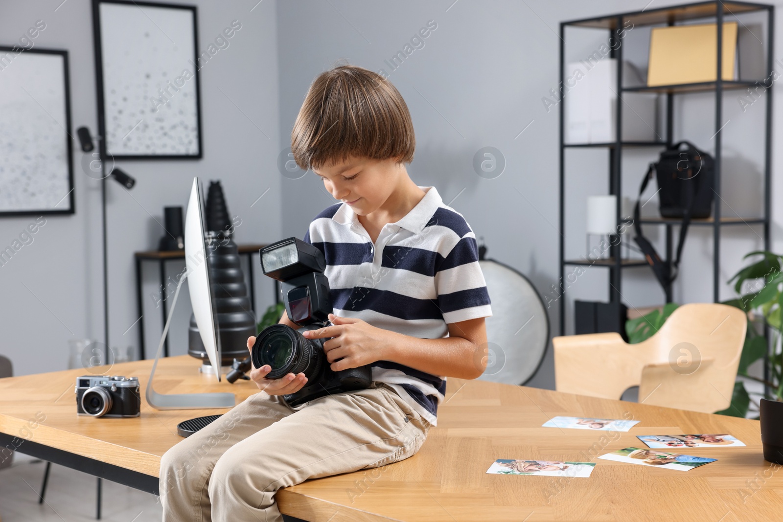 Photo of Choice of profession. Little boy with camera pretending to be photographer on wooden table in studio