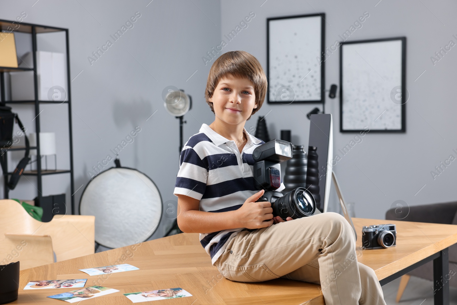 Photo of Choice of profession. Little boy with camera pretending to be photographer on wooden table in studio