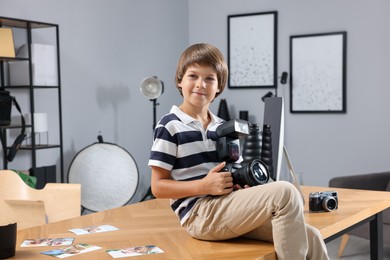 Photo of Choice of profession. Little boy with camera pretending to be photographer on wooden table in studio