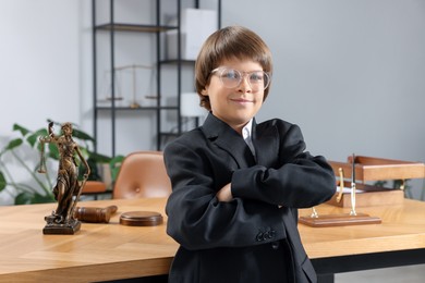 Photo of Choice of profession. Little boy in glasses and suit pretending to be lawyer near wooden table in office