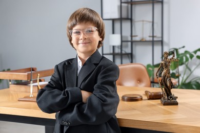 Photo of Choice of profession. Little boy in glasses and suit pretending to be lawyer near wooden table in office