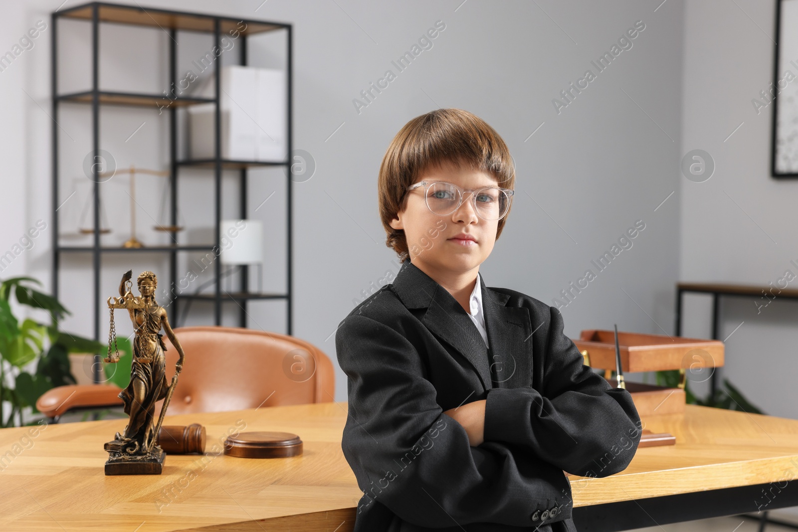 Photo of Choice of profession. Little boy in glasses and suit pretending to be lawyer near wooden table in office