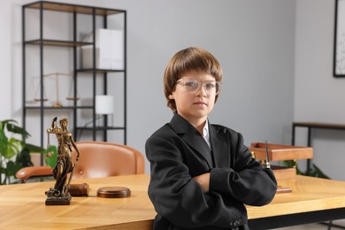 Photo of Choice of profession. Little boy in glasses and suit pretending to be lawyer near wooden table in office