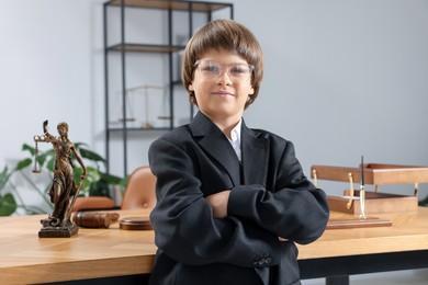 Photo of Choice of profession. Little boy in glasses and suit pretending to be lawyer near wooden table in office