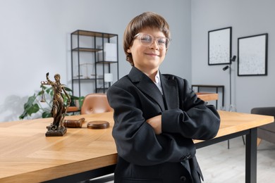 Photo of Choice of profession. Little boy in glasses and suit pretending to be lawyer near wooden table in office