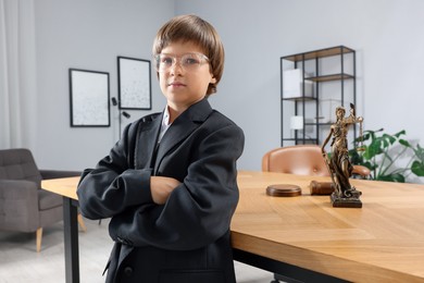 Photo of Choice of profession. Little boy in glasses and suit pretending to be lawyer near wooden table in office
