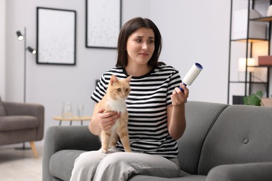 Photo of Woman with lint roller and her cat on sofa at home