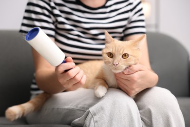 Photo of Woman with lint roller and her cat on sofa at home, closeup