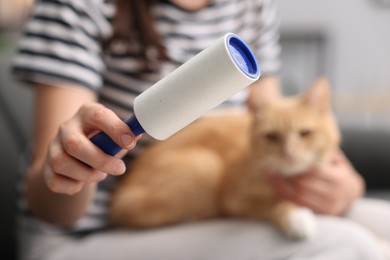 Photo of Woman with lint roller and her cat at home, selective focus