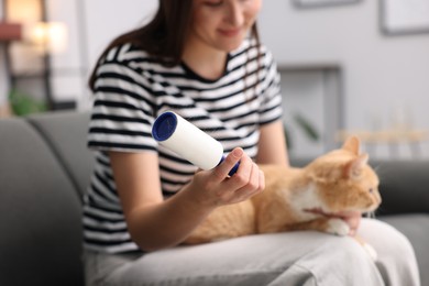 Photo of Woman with lint roller and her cat on sofa at home, selective focus