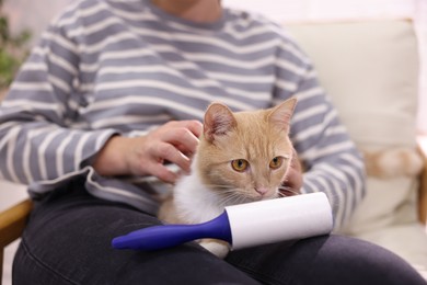Photo of Woman with lint roller and her cat on armchair at home, closeup
