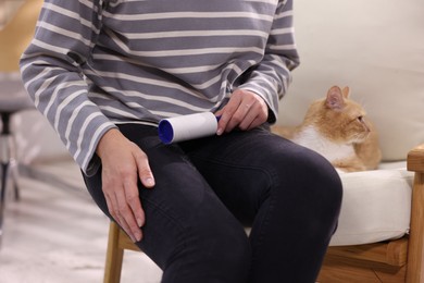 Photo of Woman with lint roller removing pet's hair from pants and her cat on armchair at home, closeup