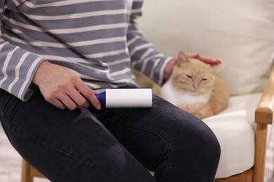 Photo of Woman with lint roller stroking her cat on armchair, closeup