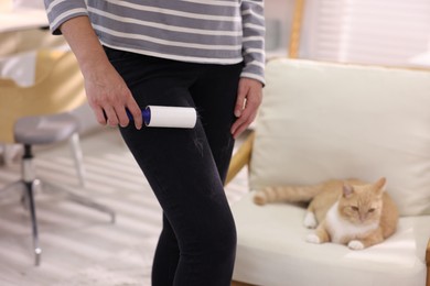 Photo of Woman with lint roller removing pet's hair from pants and her cat on armchair at home, closeup