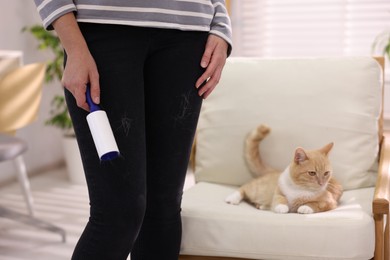 Photo of Woman with lint roller removing pet's hair from pants and her cat on armchair at home, closeup