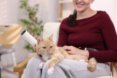 Photo of Smiling woman with lint roller stroking her cat on armchair at home, closeup