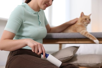 Photo of Woman with lint roller removing pet's hair from pants and stroking her cat on bench at home, closeup
