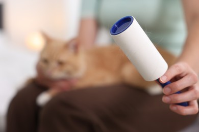Photo of Woman with lint roller and her cat at home, selective focus