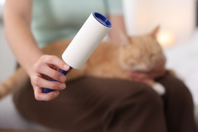 Photo of Woman with lint roller and her cat at home, selective focus
