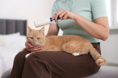 Photo of Woman rubbing down her cat with lint roller at home, closeup