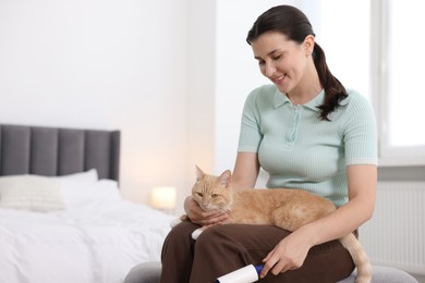 Photo of Smiling woman with lint roller and her cat on bench in bedroom. Space for text
