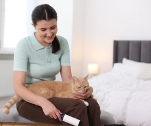 Photo of Smiling woman with lint roller and her cat on bench in bedroom. Space for text