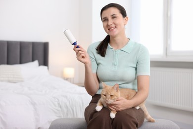 Photo of Smiling woman with lint roller and her cat on bench in bedroom. Space for text
