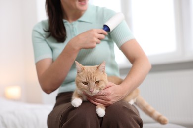 Photo of Woman with lint roller removing pet's hair from clothes and her cat at home, closeup