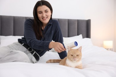 Photo of Smiling woman rubbing down her cat with lint roller on bed at home